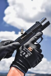 Detailed image of gloved hands reloading a pistol against a bright sky background.