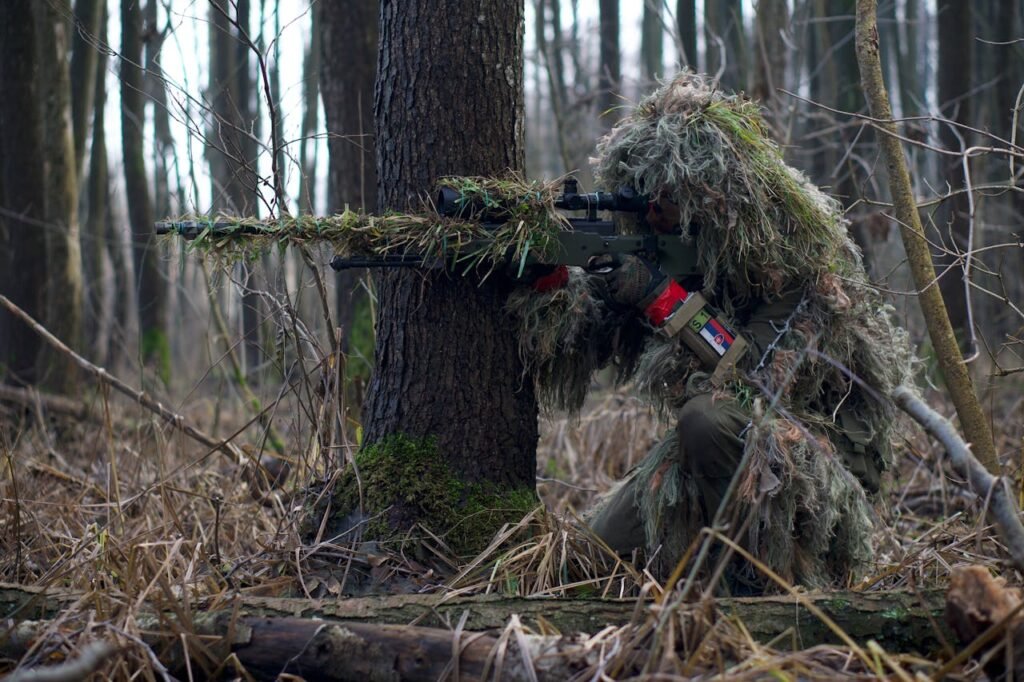 Sniper in camouflage gear taking aim in a dense forest environment.