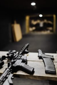 Assault rifles and handguns on a table at an indoor shooting range.